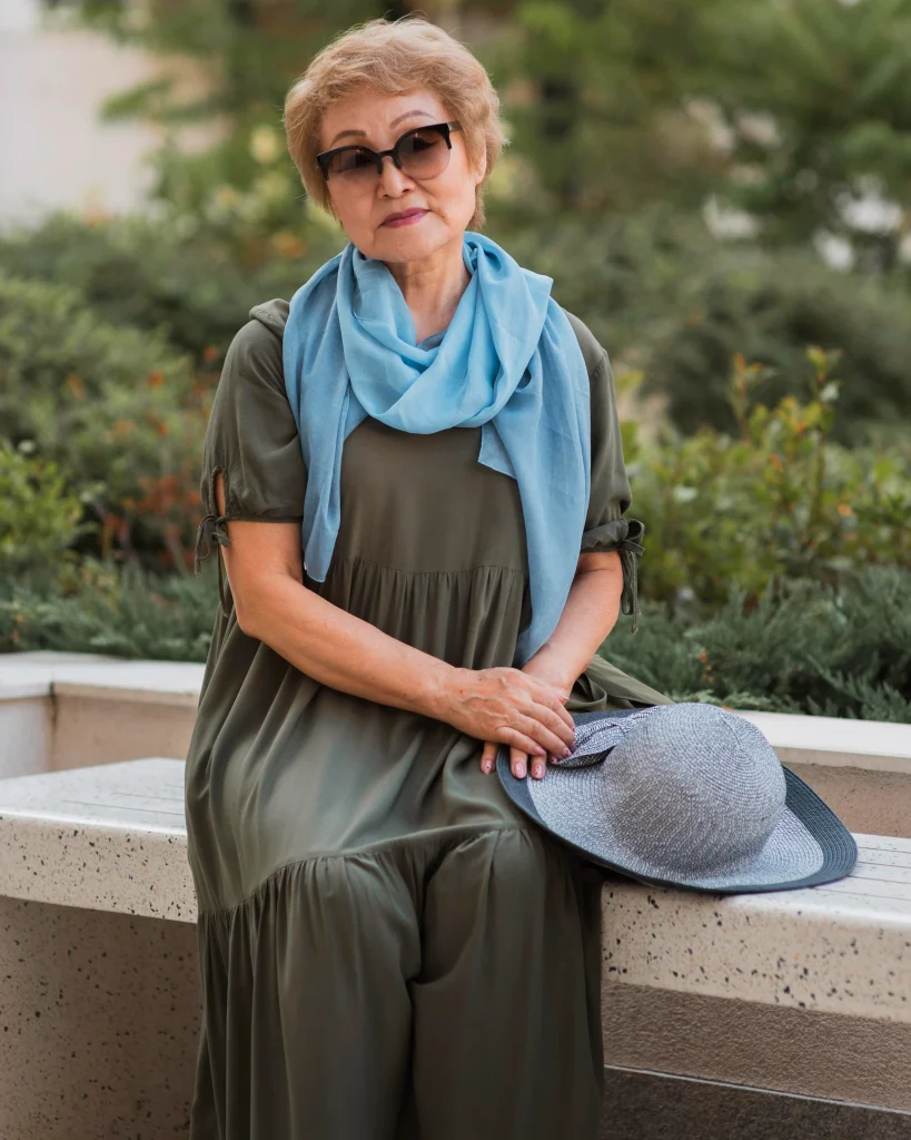 front view of a stylish elderly woman seated, wearing a cardigan, neutral background